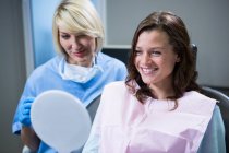 Усміхнений пацієнт дивиться у дзеркало з стоматологом, що сидить на ній — стокове фото
