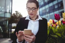 Молода бізнес-леді, використовуючи мобільний телефон за квітами — стокове фото
