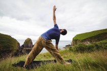 Rear view of man performing stretching exercise on cliff — Stock Photo