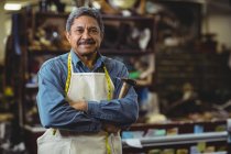 Confident shoemaker standing with arms crossed in workshop — Stock Photo