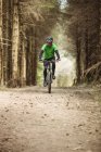 Vista frontal del ciclista de montaña que monta en el camino de tierra en el bosque - foto de stock