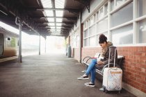 Молода жінка використовує телефон, сидячи на вокзалі — стокове фото