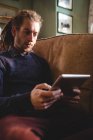 Jeune homme hipster utilisant une tablette numérique sur le canapé à la maison — Photo de stock
