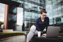 Young businesswoman using laptop against modern building — Stock Photo