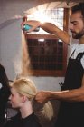 Coiffeur masculin coiffant les cheveux des clients avec de la laque au salon — Photo de stock