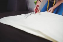 Cropped image of Female fashion designer cutting white fabric in studio — Stock Photo