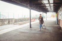 Longitud total de la mujer que lleva equipaje mientras camina en la plataforma de la estación de tren - foto de stock