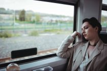 Mujer cansada sentada junto a la ventana en tren - foto de stock