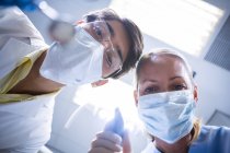 Dentist and dental assistant in surgical masks holding dental tools in dental clinic — Stock Photo