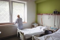 Старша жінка стоїть біля вікна в лікарні — стокове фото