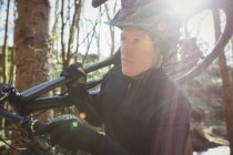 Чоловічий гірський велосипедист, що перевозить велосипед деревами в лісі — стокове фото