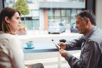 Homem usando telefone celular enquanto conversa com mulher na cafetaria — Fotografia de Stock