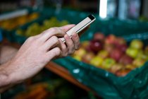 Imagem cortada do homem usando smartphone enquanto faz compras no supermercado — Fotografia de Stock