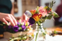 Close-up de flores em garrafa, enquanto florista feminino preparando buquê de flores no fundo — Fotografia de Stock