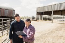 Farmer and vet looking in clipboard against barn on sunny day — Stock Photo