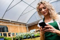 Жіночий флорист, використовуючи мобільний телефон в садовому центрі — стокове фото