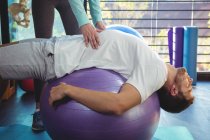 Female physiotherapist helping male patient on exercise ball in clinic — Stock Photo