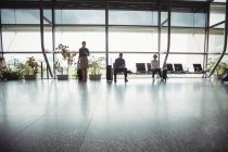 Business people sitting with luggage at waiting area in airport terminal — Stock Photo