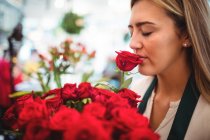 Fiorista donna che annusa un fiore di rosa nel negozio di fiori — Foto stock