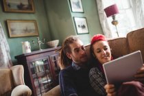 Casal jovem usando tablet digital no sofá em casa — Fotografia de Stock