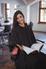 Портрет улыбающейся женщины, сидящей на стуле и читающей журнал в парикмахерской — стоковое фото