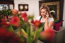 Женщина-флорист с ноутбуком во время разговора по мобильному телефону в цветочном магазине — стоковое фото