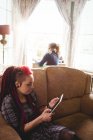 Jeune femme hipster utilisant une tablette numérique tout en étant assis sur le canapé à la maison — Photo de stock