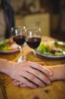 Пара тримає руки вдома за столом з келихами для вина — стокове фото