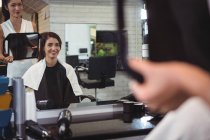 Sorrindo cabeleireiro feminino mostrando mulher seu corte de cabelo no espelho no salão — Fotografia de Stock