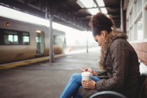Mulher usando telefone enquanto sentado na estação ferroviária — Fotografia de Stock
