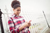 Hübsche junge Frau benutzt Handy, während sie sich an Geländer lehnt — Stockfoto
