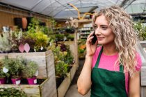 Женщина-флористка разговаривает по мобильному телефону в садовом центре — стоковое фото