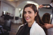 Lächelnde Friseurin zeigt Frau im Salon ihren Haarschnitt im Spiegel — Stockfoto