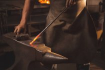 Schmied im mittleren Abschnitt bearbeitet heißes Metall mit Hammer in der Werkstatt — Stockfoto