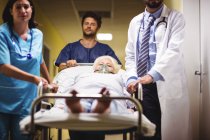 Лікар і медсестра штовхають старшого пацієнта на ноша в лікарняному коридорі — стокове фото