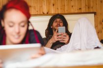 Жінка розслабляється з чоловіком, використовуючи мобільний телефон на ліжку вдома — стокове фото