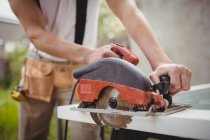Midsection of carpenter cutting wooden frame from circular saw on lawn — Stock Photo