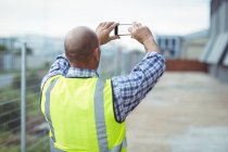 Construction worker photographing with mobile phone outside office — Stock Photo