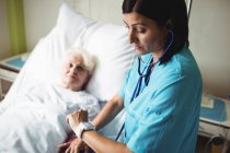 Enfermera revisando la presión arterial del paciente mayor en el hospital - foto de stock