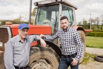 Portrait of men standing by tractor at farm — Stock Photo