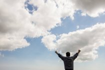 Visão traseira do homem com os braços erguidos contra o céu nublado — Fotografia de Stock