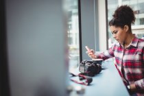 Молода жінка використовує мобільний телефон, сидячи в ресторані — стокове фото