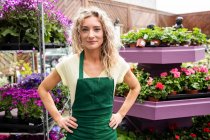 Portrait of female florist standing with hands on hips in garden centre — Stock Photo