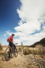 Motociclista de pé com bicicleta na estrada de terra na montanha — Fotografia de Stock