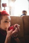 Junge Hipster-Frau trinkt Kaffee, während sie zu Hause auf dem Sofa sitzt — Stockfoto