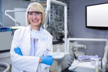 Portrait d'un dentiste souriant debout les bras croisés à la clinique dentaire — Photo de stock