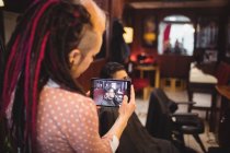 Female barber taking photo of client from digital tablet in barber shop — Stock Photo