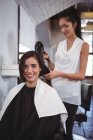 Retrato de mujer secándose el pelo con secador de pelo en la peluquería - foto de stock