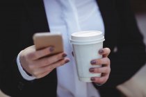 Midsection de mulher segurando telefone celular e copo de café descartável — Fotografia de Stock