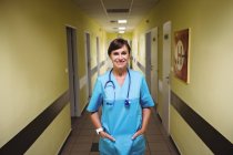 Retrato de enfermera de pie con las manos en el bolsillo en el pasillo del hospital - foto de stock